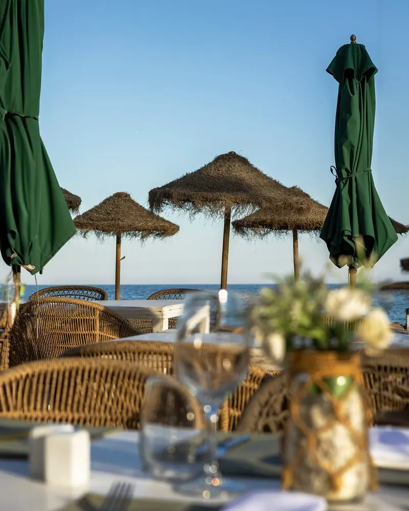 Las Cuchis table under green parasols and palm-leaf umbrellas on the beach