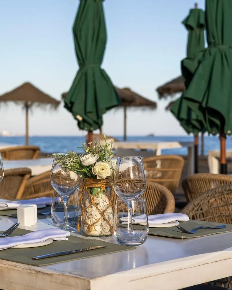 Flowers and glassware on a table at Las Cuchis, with the beach behind